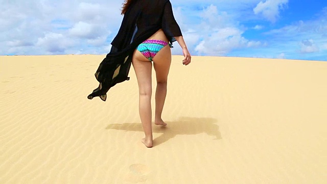 一个女孩穿着泳衣在富埃特文图拉岛的沙丘上散步，微风吹拂着她的裙子，伴随着令人惊叹的风景。视频下载