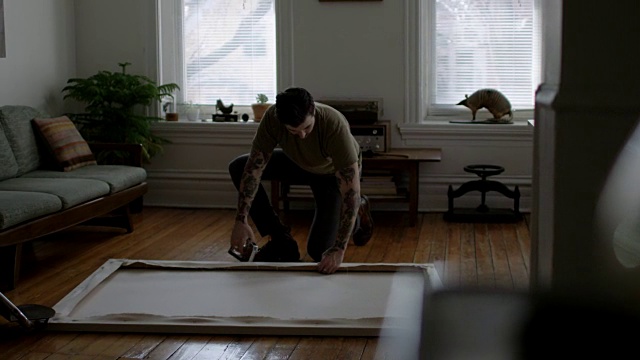 年轻的纹身艺术家WS SLO用钉枪在公寓地板上组装一张拉伸的画布。视频素材