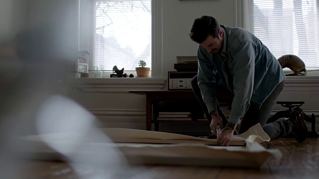 年轻的DIY艺术家WS SLO在公寓地板上用钉书枪在木框架上折叠和装订帆布。视频素材