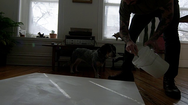 当画家用画笔在画布上涂抹底漆时，一只好奇的狗来回晃动着头。视频素材