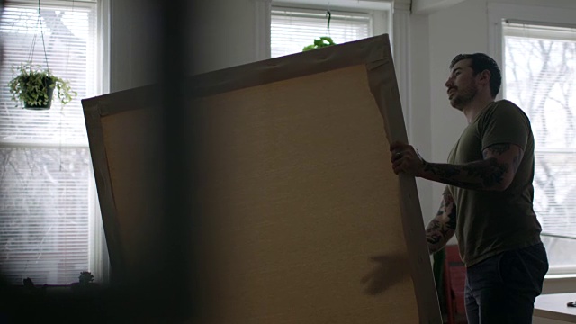 年轻艺术家WS SLO MO在阳光城市的公寓刷出并检查空白画布。视频素材