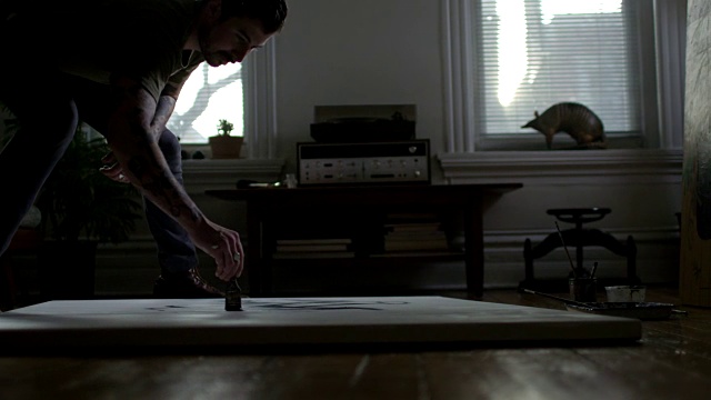 年轻的艺术家斜靠在画布上，在公寓的地板上用粗线条作画。视频素材