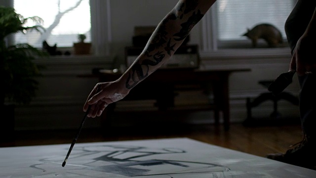 年轻的艺术家斜倚在公寓地板上的画布上，用复杂的笔触作画。视频素材