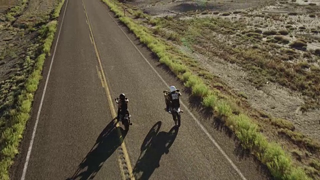 两个人骑着摩托车在沙漠公路上行驶，鸟瞰图视频素材