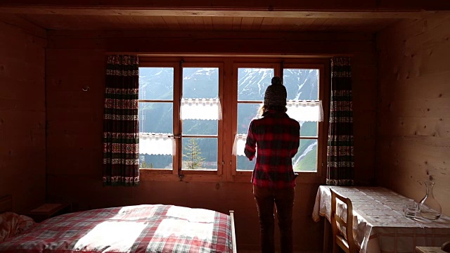 在瑞士阿尔卑斯山，一名女子用手机从她的小木屋的窗户里拍照。视频下载