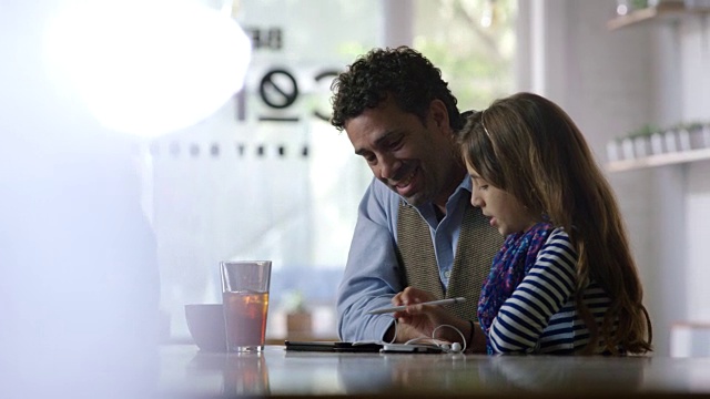 小女孩向父亲展示如何在现代咖啡店使用平板电脑。视频素材
