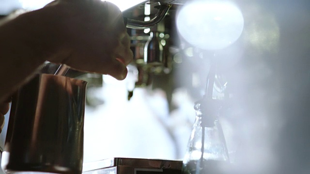 咖啡店的咖啡师转动旋钮，将牛奶和蒸汽搅起泡沫，制作卡布奇诺。视频素材