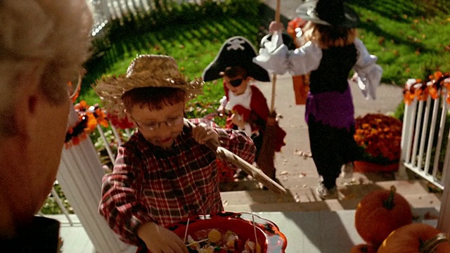 中等镜头的女人拿着一碗糖果，孩子们穿着戏服来到门前/宾夕法尼亚州视频下载