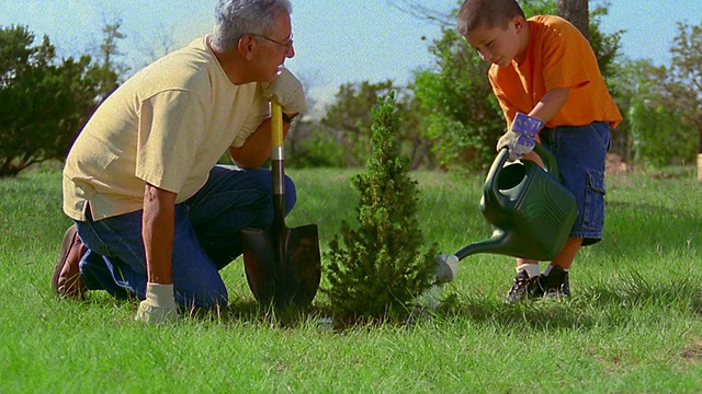 新墨西哥，一个西班牙男孩在给灌木浇水，另一个男人在室外观看视频素材