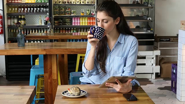 年轻女子一边喝咖啡一边用平板电脑视频素材