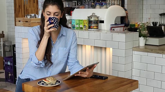 女性顾客一边喝咖啡一边用平板电脑视频素材