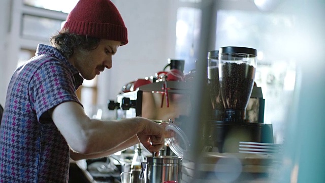 在现代咖啡店里，年轻的咖啡师用勺子往咖啡里加糖。视频下载