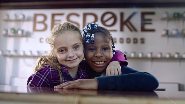 两个可爱的小女孩对着镜头微笑，在当地的咖啡店里大笑。视频素材