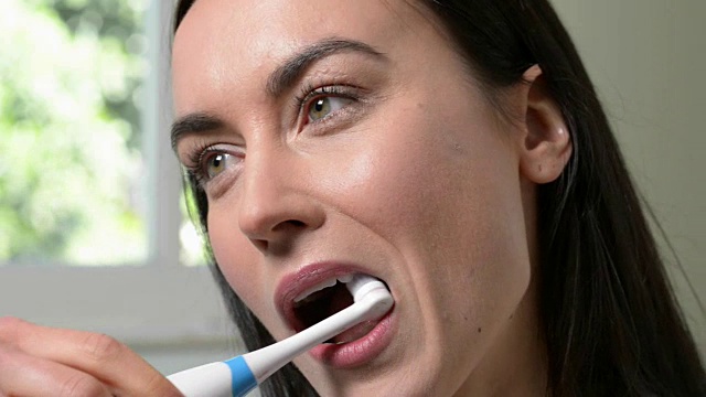 在浴室用电动牙刷刷牙的女人视频素材