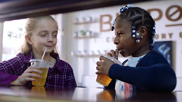 小女孩们在当地的咖啡店喝着苹果汁，对着镜头微笑。视频素材