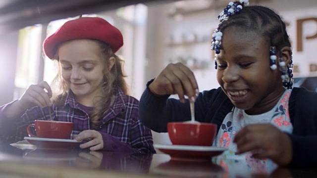 在咖啡店里，小女孩们在杯子里搅拌热巧克力，啜饮勺子。视频素材