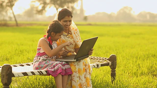 在印度哈里亚纳邦的农场里，一名成年妇女教她的女儿使用电脑视频素材