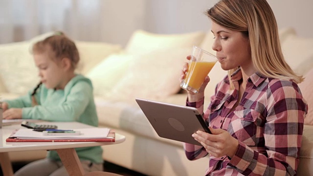 年轻的母亲用触控板上网，在家喝橙汁。视频素材