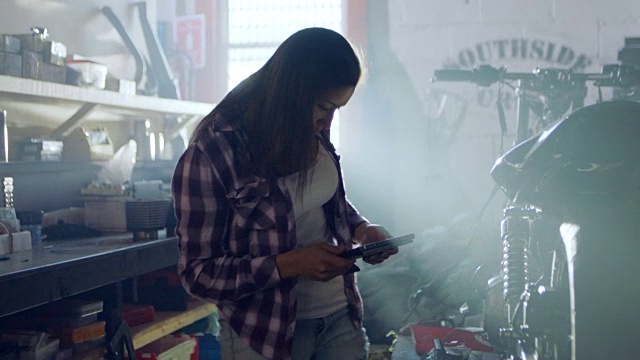 女机械师在现代汽车修理厂学习平板电脑和摩托车。视频素材
