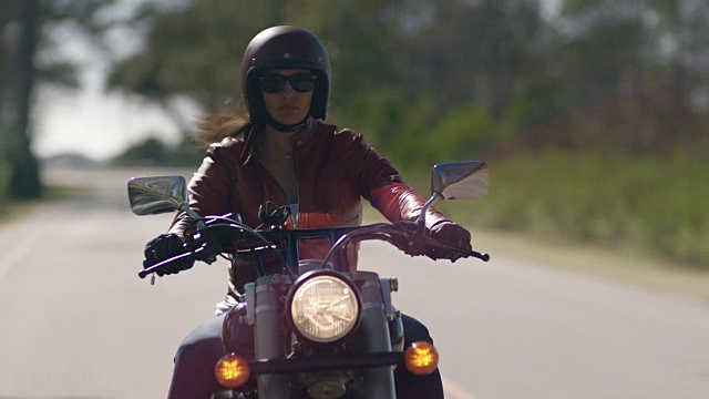 骑摩托车的女孩穿着皮夹克，骑着摩托车在空旷的路上行驶。视频下载