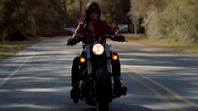 骑摩托车的女孩穿着皮夹克，骑着摩托车在崎岖不平的乡村公路上飞驰。视频素材