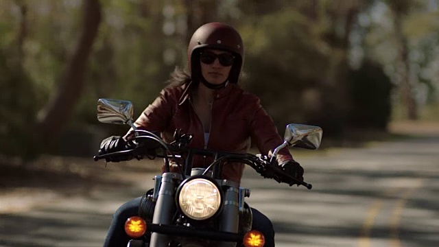 骑摩托车的女孩穿着皮夹克在弯弯曲曲的道路上行驶。视频下载