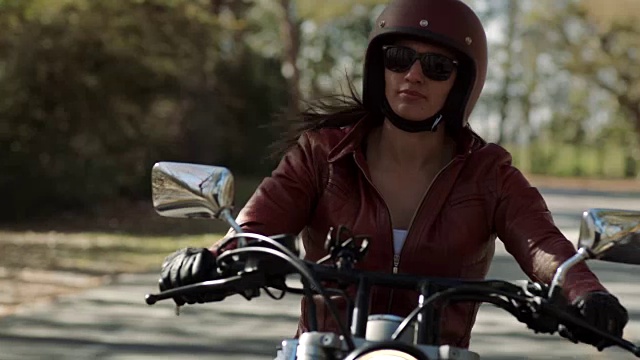 女人骑着摩托车在空旷的路上行驶，在阳光明媚的森林大道上转弯。视频素材