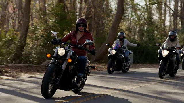 SLO MO:骑摩托车的女孩团伙在树木繁茂的高速公路上用手势交流。视频素材