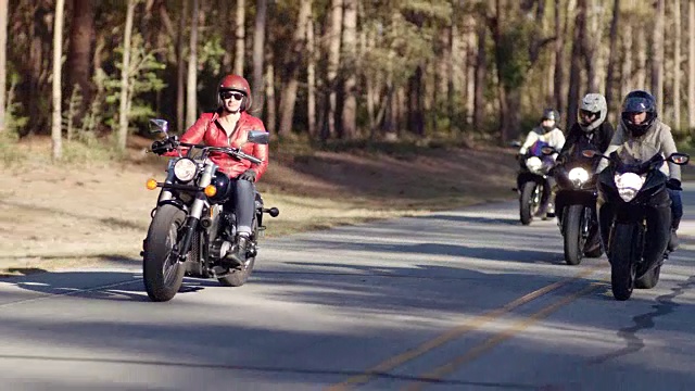 四名女子骑着摩托车在林木茂盛的公路上列队行驶。视频素材