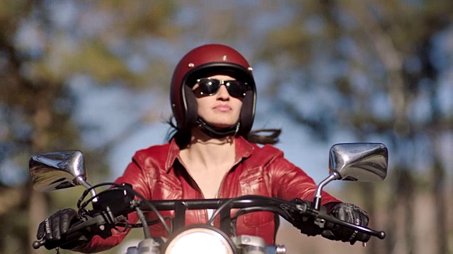 年轻女子骑摩托车在阳光大道的大树下巡游。视频素材