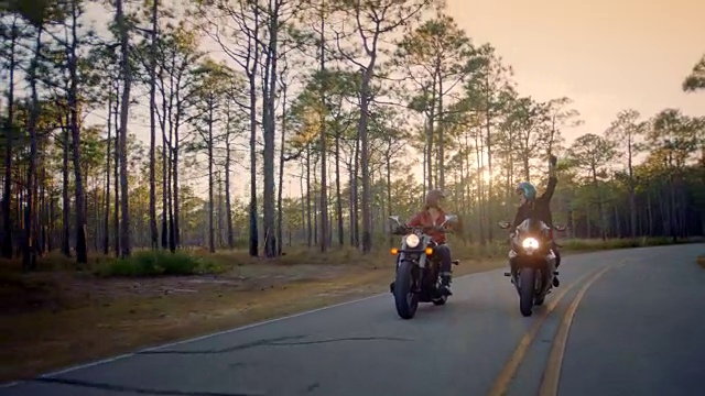 两个骑摩托车的女人在日落大道上挥拳相向。视频素材