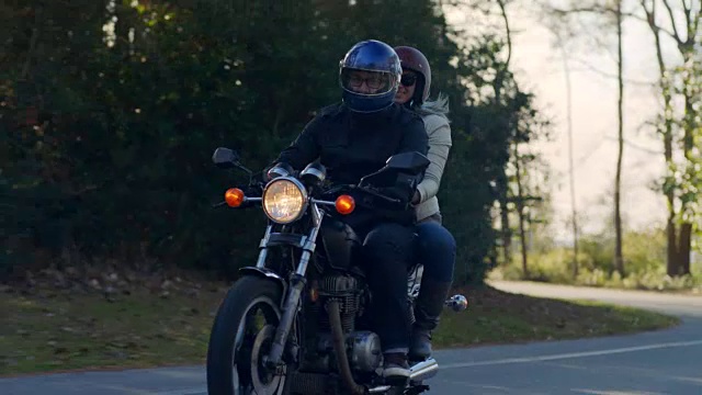 阳光穿过树木，快乐的夫妇驾驶着摩托车沿着森林道路。视频素材