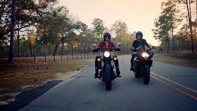 两个女人骑着摩托车穿过国家公园森林，在公路旅行中一起欢笑。视频素材