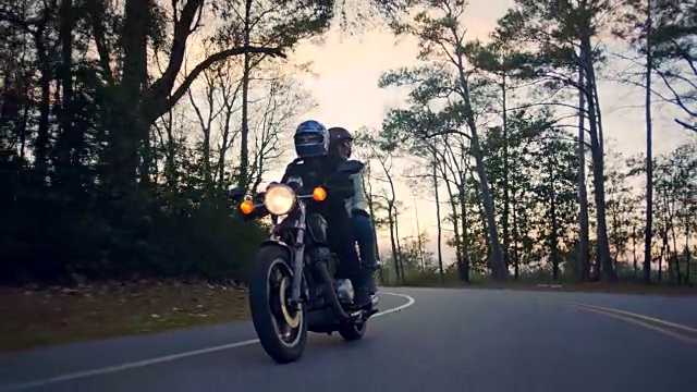 快乐的年轻夫妇骑着摩托车沿着弯曲的森林路行驶。视频素材