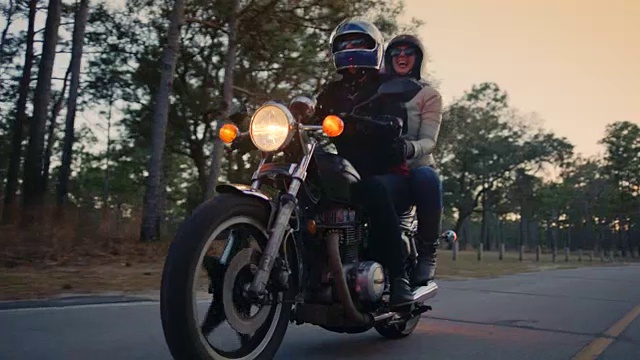 快乐的年轻夫妇骑摩托车经过公园大道。视频下载
