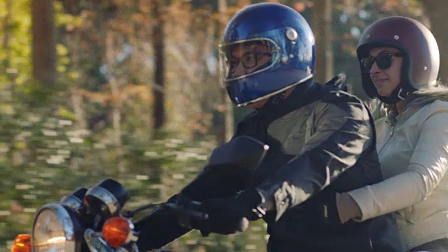 一对快乐的情侣骑着摩托车在森林路上巡游。视频素材