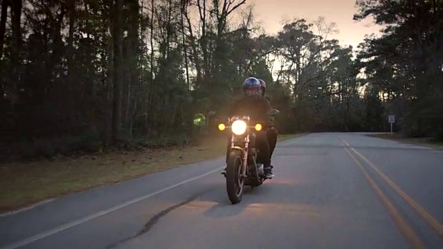 一对年轻的夫妇晚上在孤独的森林道路上驾车，摩托车前灯闪耀。视频素材