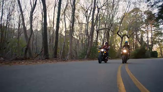 两个女人骑着摩托车并排笑着，沿着幽静的森林公路行驶。视频下载