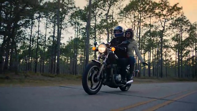 SLO MO。女孩在摩托车的后面在空中挥舞手臂的男朋友开车在森林公路上的公路旅行。视频下载