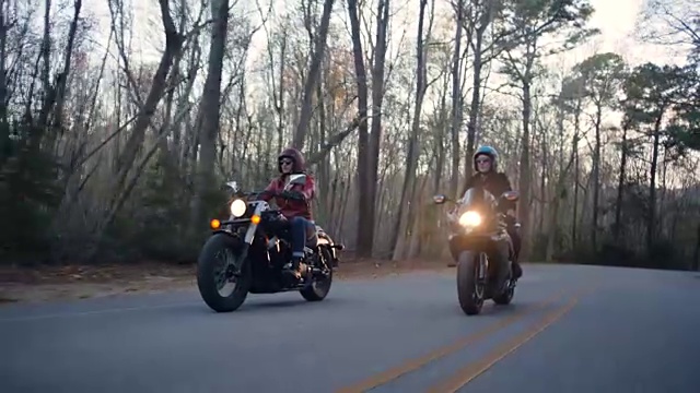 三名女子骑着摩托车在蜿蜒曲折的森林公路上列队行驶。视频素材