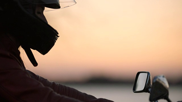 女子放下头盔上的遮阳帽，在风景优美的河边骑上摩托车。视频下载
