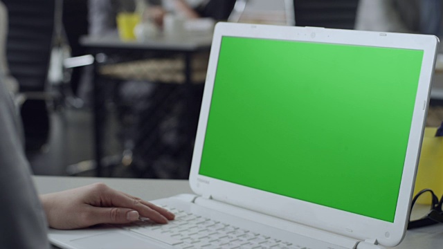 在办公室用绿色屏幕的笔记本电脑工作的女性视频下载