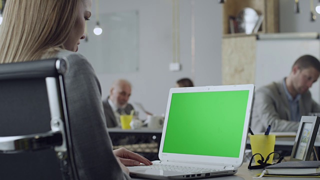 在办公室用绿色屏幕的笔记本电脑工作的女性视频下载
