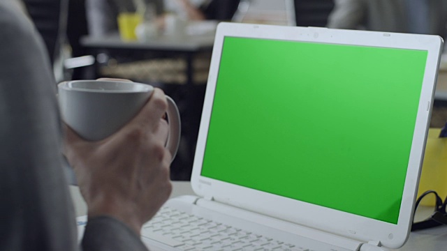 女性端着咖啡，在办公室用绿色屏幕的笔记本电脑工作视频下载
