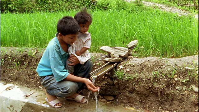 中等拍摄的男孩抱着孩子在粗糙的水源冲洗他的手/尼泊尔视频素材
