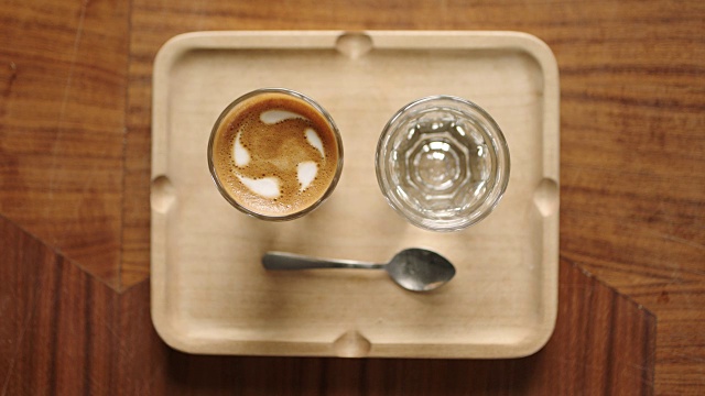 头顶上放着一杯浓缩咖啡，水杯和勺子放在时髦的咖啡馆的木托盘上。视频素材