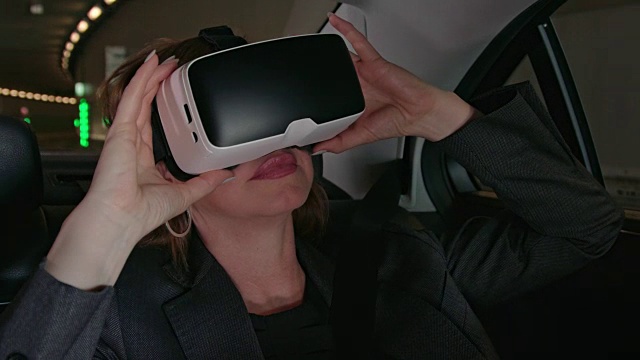 40多岁的成熟商业女性，一头棕色的长发，在一辆豪华轿车的司机的陪同下穿过城市/与出租车通过隧道，同时使用VR耳机视频下载