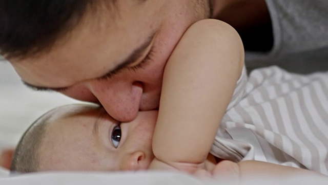 爸爸亲吻躺在床上的男婴的脸颊视频素材