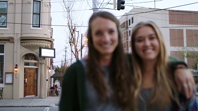 两名年轻女子对着镜头微笑，照片摄于市中心一家咖啡店外的街角。视频素材