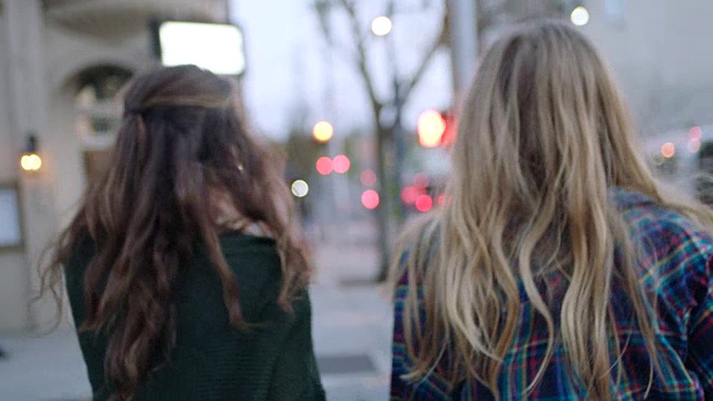 两个女孩穿过城市街道，走进市中心时尚街区的一家咖啡店。视频素材